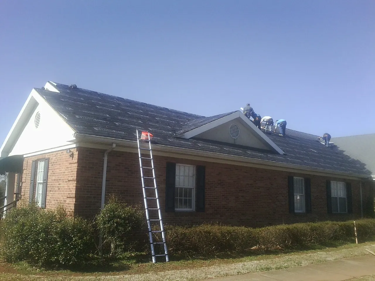 Crew tearing shingles off a brick ranch roof with a ladder set — Metal Roof Repair work by our crew in Usk