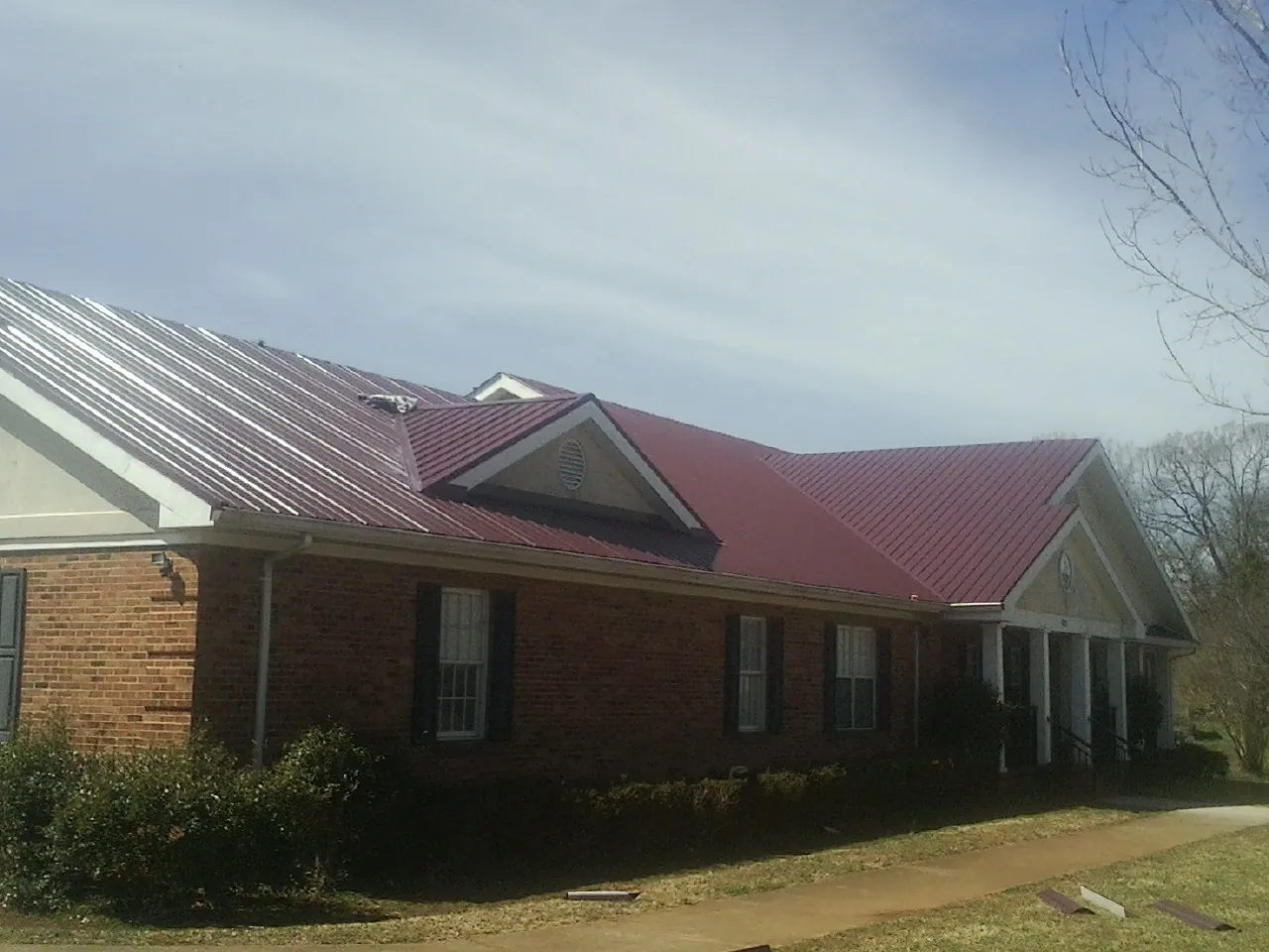 Red metal roof with gabled entries on a long brick building, from a Hail Damage Roof Repair job in Usk