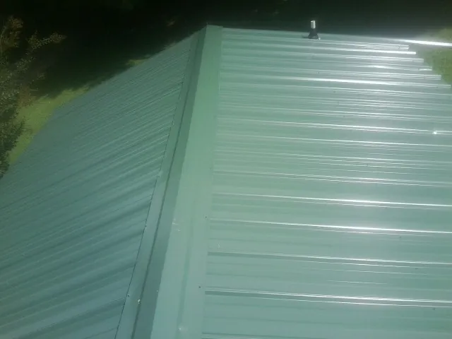 New green metal panels meeting at the ridge of a roof — Flat Roof Repair work by our crew in Usk