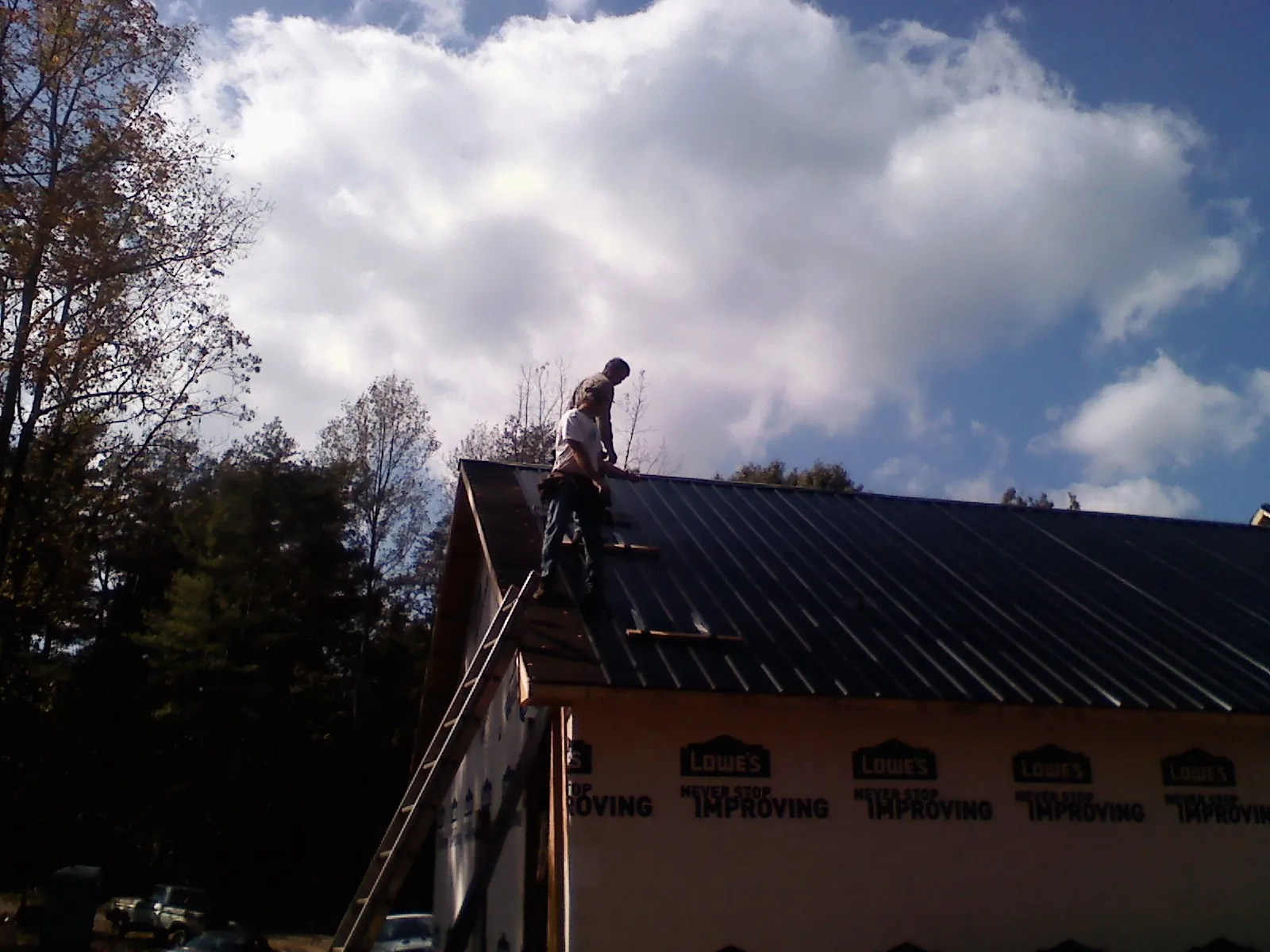 Roofer fastening dark metal panels high against a cloudy sky, from a Roof Inspection job in Usk