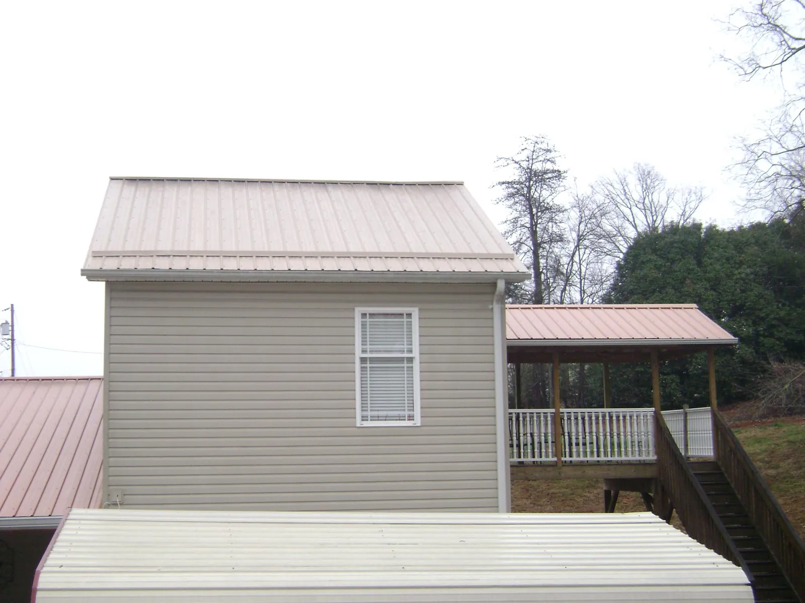 Tan metal roofs on a two story addition and attached porch, from a Roof Replacement job in Usk